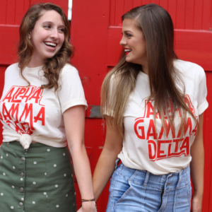 Two members standing in front of a red doorway holding hands. They are wearing matching shirts.