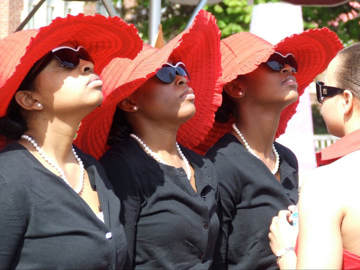 Three members of Delta Sigma Theta  in red sun hats look up.